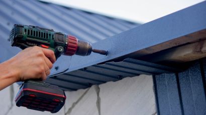 Close-up view of a builder’s hand fixing damaged roof shingles with an electric screwdriver