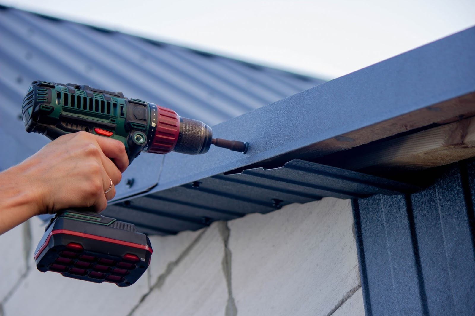 Close-up view of a builder’s hand fixing damaged roof shingles with an electric screwdriver