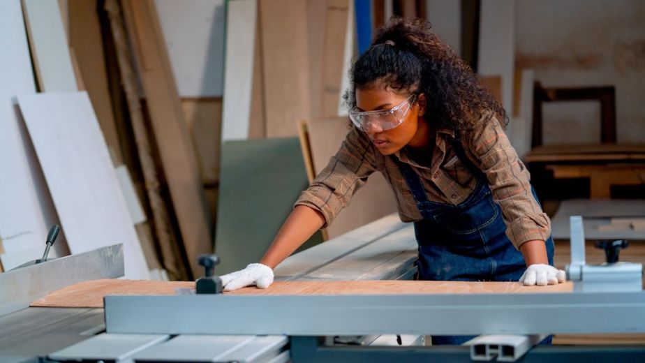 Female carpenter checking precision cutting machinery while working on custom woodworking projects