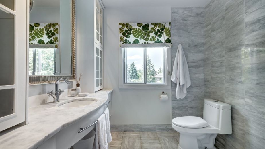 Elegantly remodeled bathroom with gray wall tiles and leaf-patterned window blinds