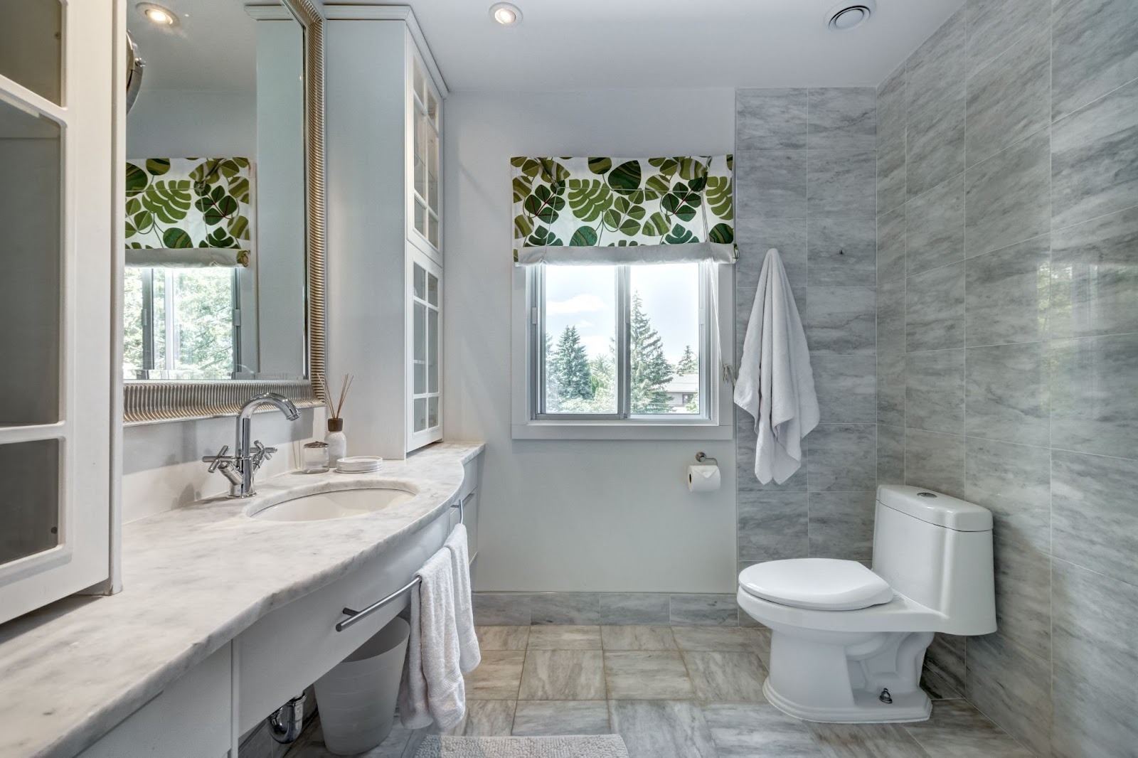 Elegantly remodeled bathroom with gray wall tiles and leaf-patterned window blinds