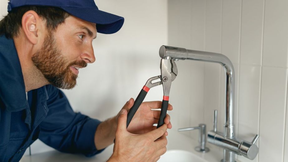 A plumber in blue workwear fixing a broken water tap in a home kitchen