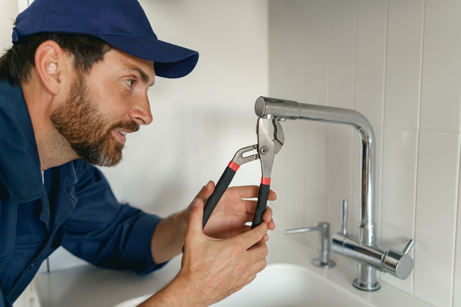 A plumber in blue workwear fixing a broken water tap in a home kitchen
