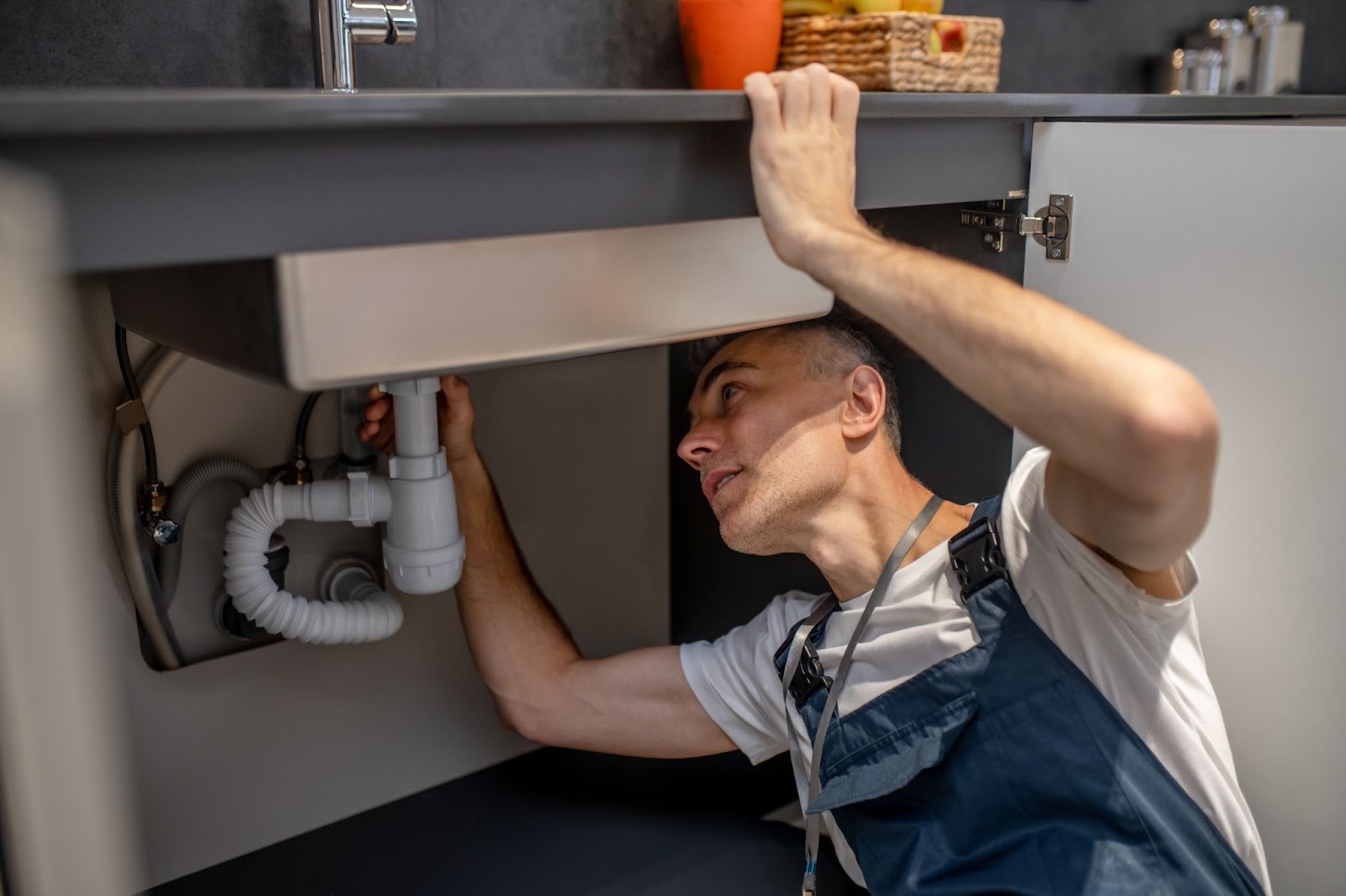 Licensed plumber examining the under-sink plumbing to diagnose a household plumbing issue