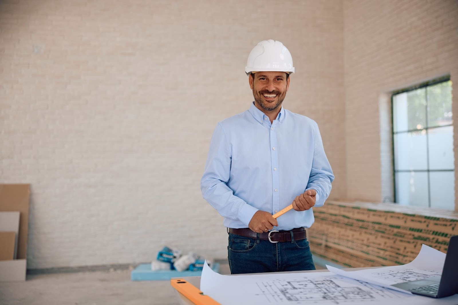 A smiling general contractor reviewing home construction plans at an active worksite
