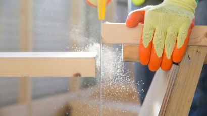A carpenter in protective gloves cutting a wooden board with a power saw
