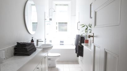 Bright all-white narrow bathroom with floating vanity, gray towels, and small plant decor for a clean, modern look