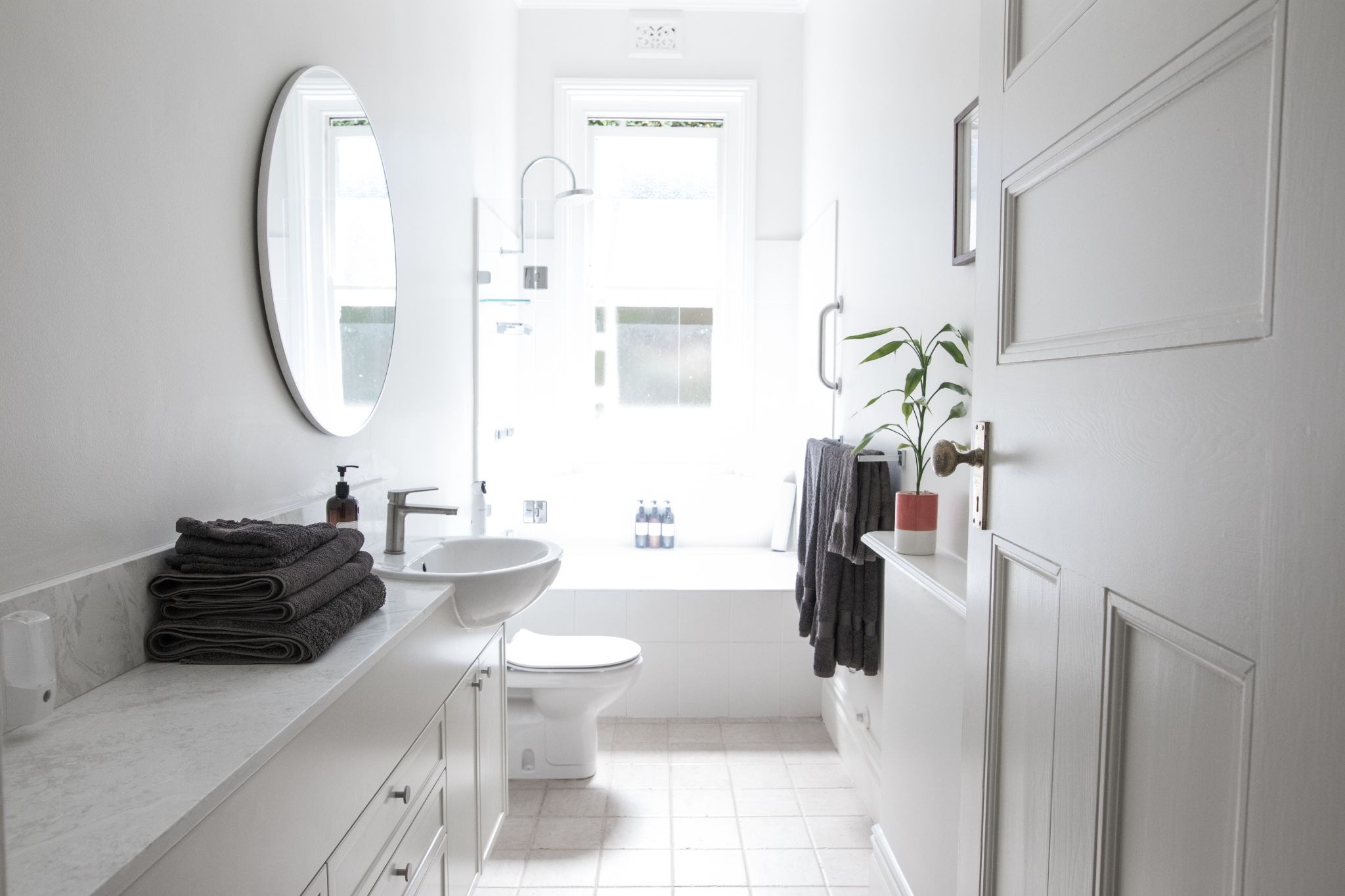 Bright all-white narrow bathroom with floating vanity, gray towels, and small plant decor for a clean, modern look