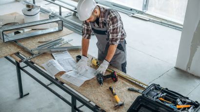 A general contractor reviewing construction blueprints on a worktable at a job site, surrounded by tools and building materials