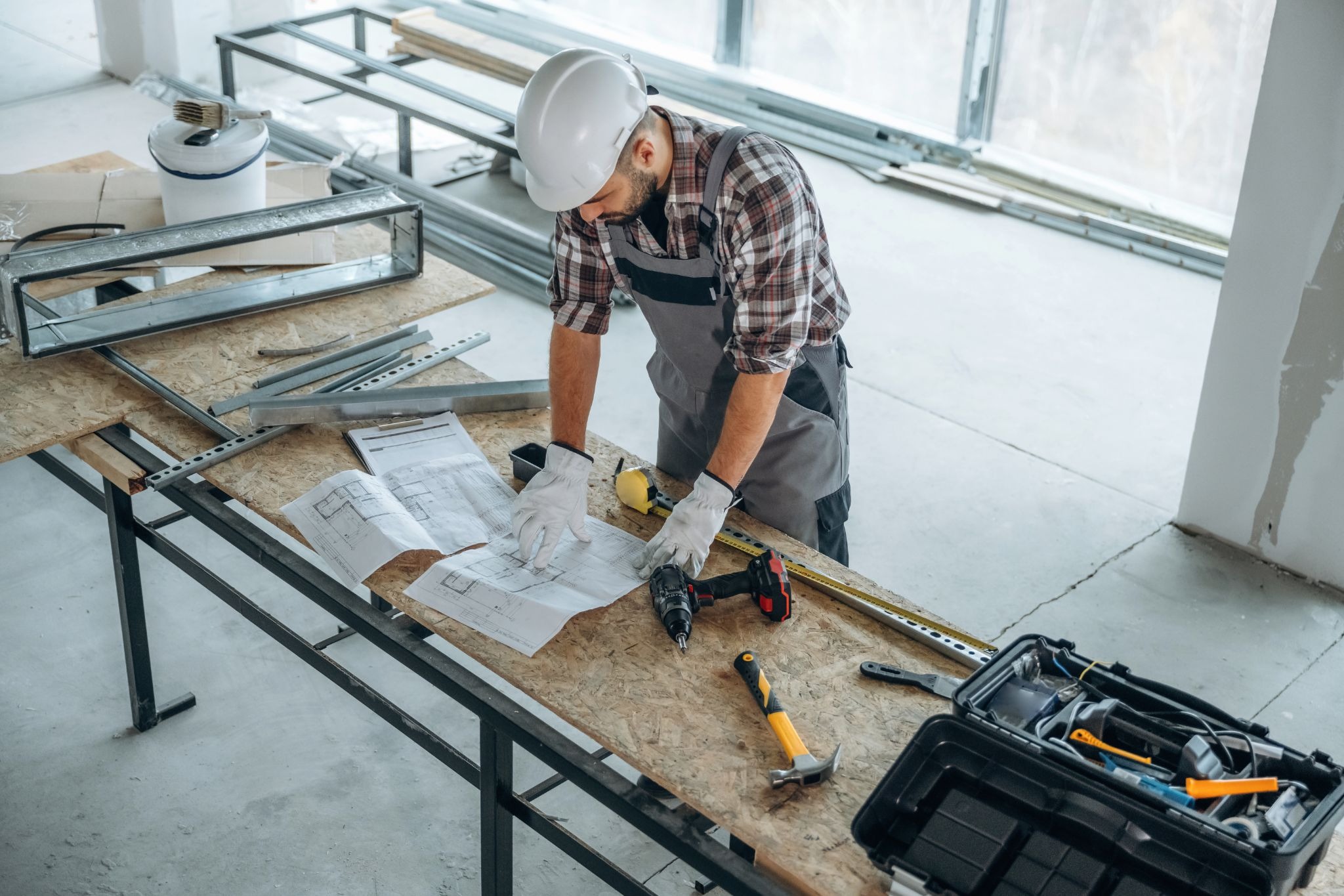 A general contractor reviewing construction blueprints on a worktable at a job site, surrounded by tools and building materials