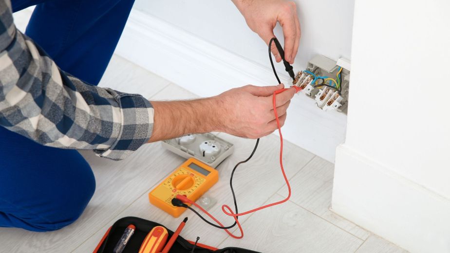 Licensed electrician performing home electrical services while checking a wall outlet with a voltage tester