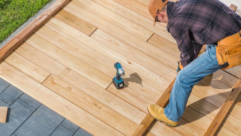 Contractor building a wooden deck using a power drill to secure boards to a sturdy outdoor frame