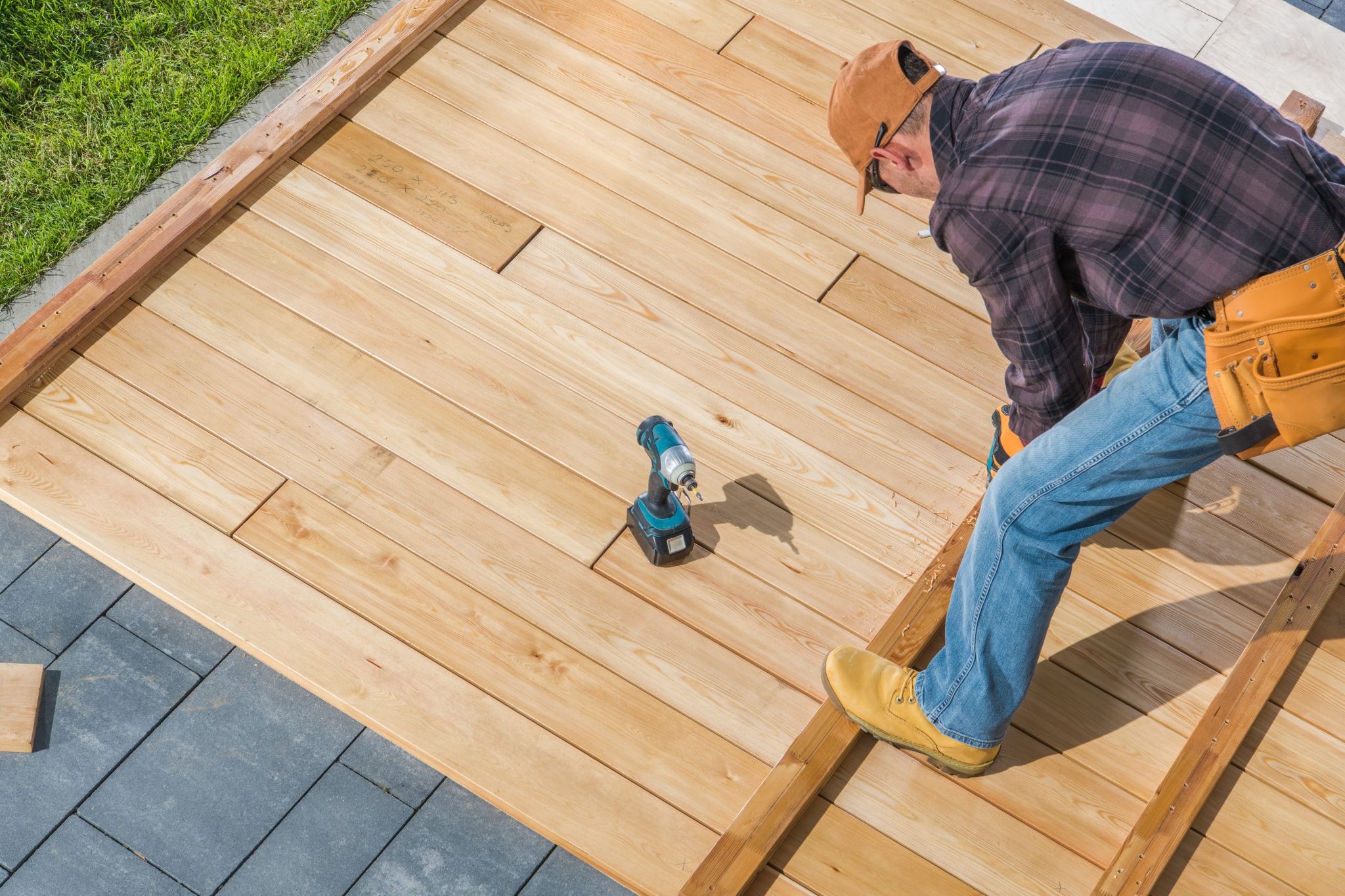 Contractor building a wooden deck using a power drill to secure boards to a sturdy outdoor frame