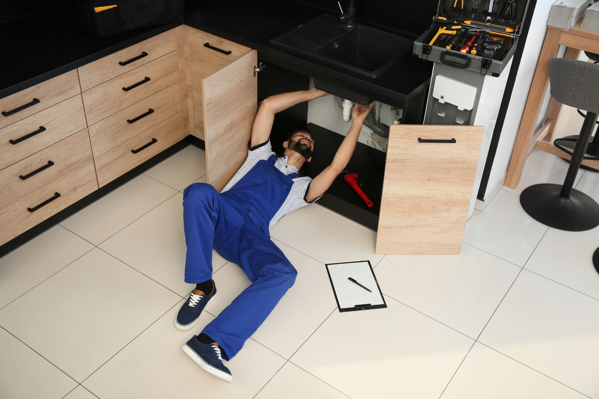 Professional plumber inspecting and repairing pipes beneath a kitchen sink cabinet